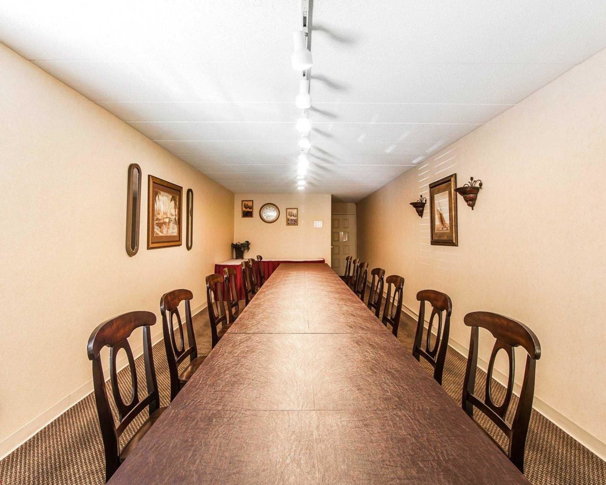 Een lange, smalle kamer met een houten tafel en stoelen, beige wanden en ingekaderde afbeeldingen.