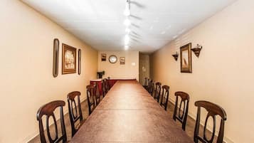 A long, narrow room with a wooden table and chairs, beige walls, and framed pictures.