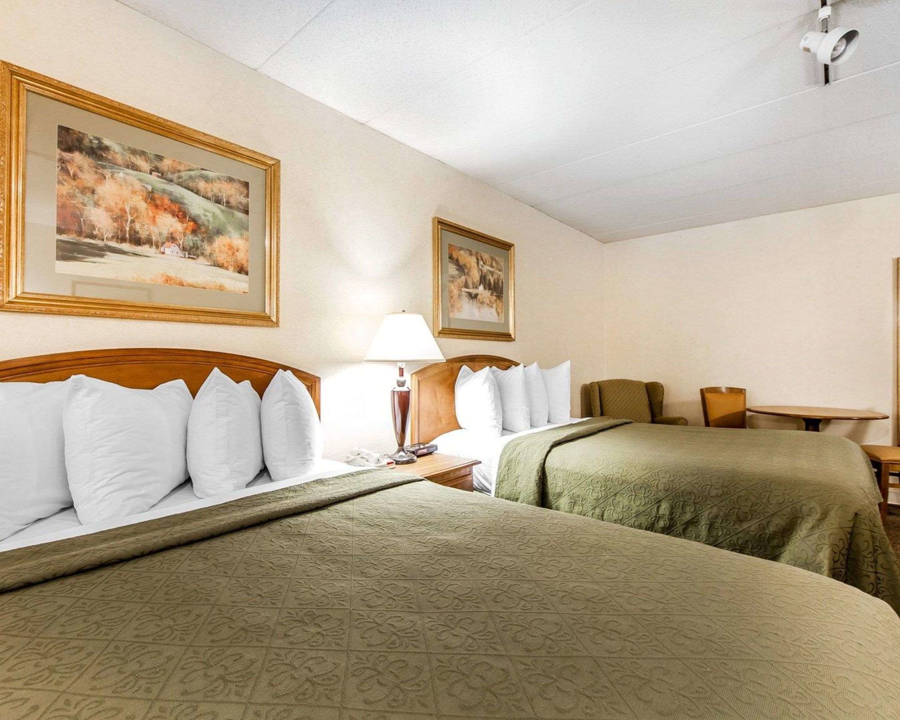 A hotel room with two beds, a nightstand, a lamp, and two framed pictures on the wall.