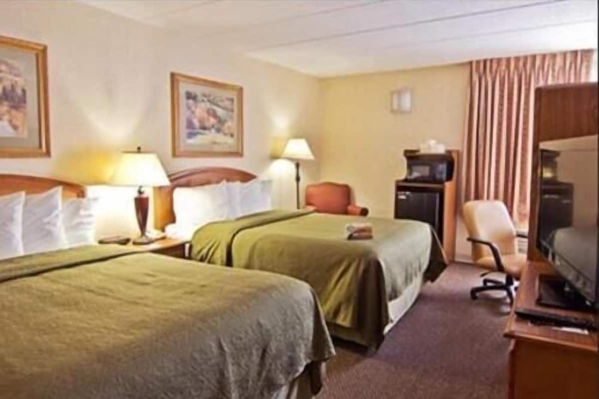 A hotel room with two beds, a desk, a chair, a television, and a lamp.