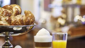 A breakfast setting with pastries, a glass of coffee, and a bowl of fruit salad.
