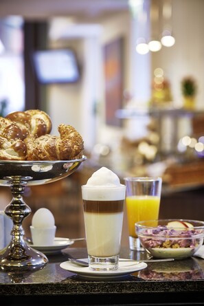 A breakfast setting with pastries, a glass of coffee, and a bowl of fruit salad.