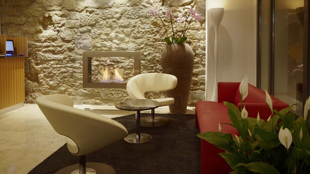 A modern interior with a stone wall, a fireplace, a white chair, a red sofa, and a vase with flowers.