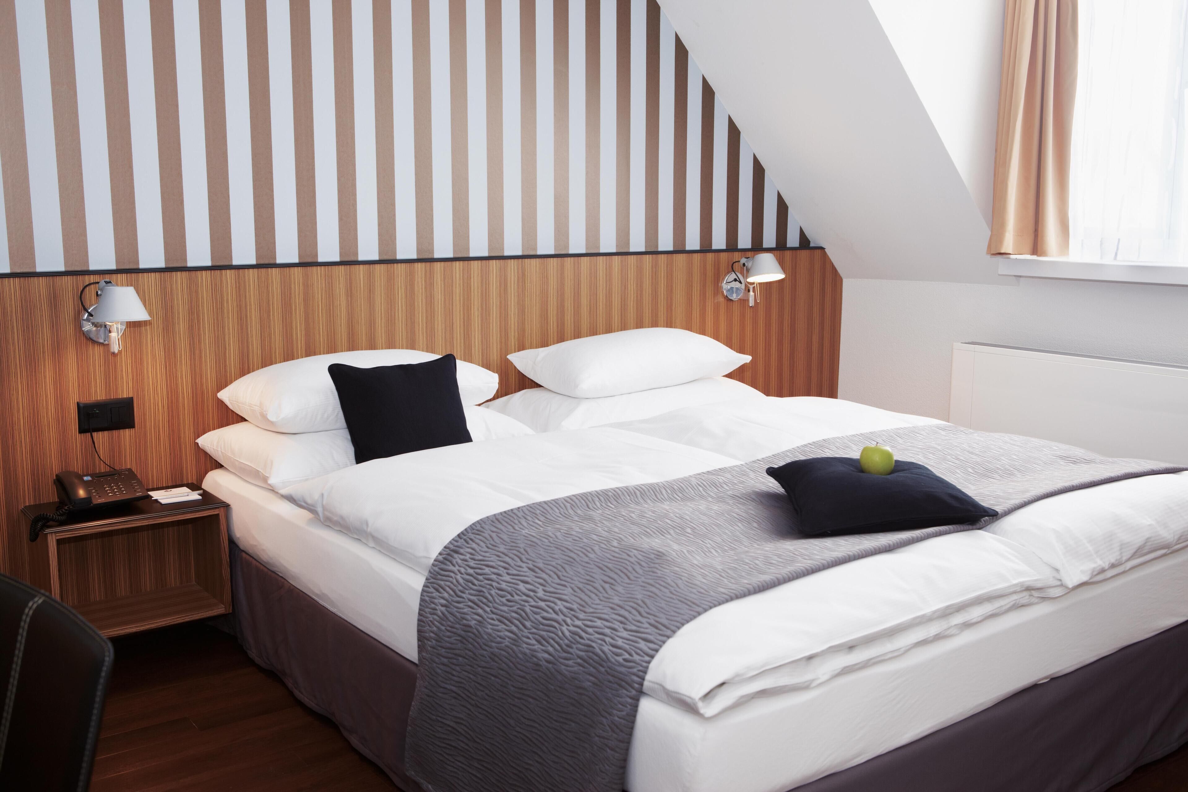 Ein Hotelzimmer mit Bett, Nachttisch, Lampe und einem Fenster mit Vorhängen.