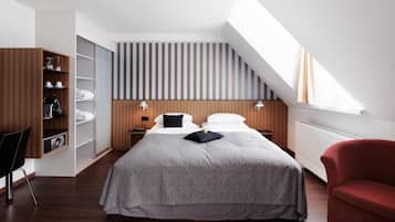 A modern bedroom with a sloped ceiling, a large bed with a grey patterned bedspread, a red armchair, and built-in wooden shelving with various items.