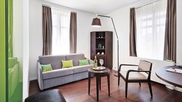 A modern living room with a grey sofa, a round table, a tall floor lamp, and a cabinet with shelves.