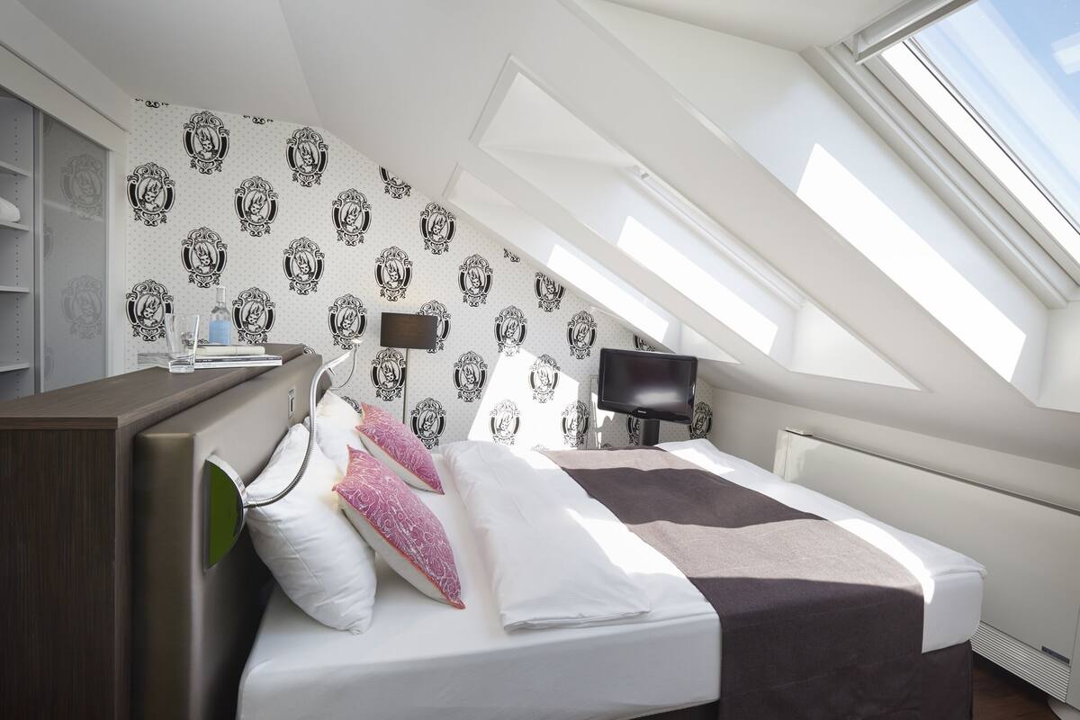 Un dormitorio moderno con tragaluz, una cama con almohadas, una mesita de noche y un televisor.