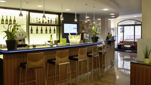 A bar area with wooden bar stools, a counter with bottles, a television screen, and a stone wall.