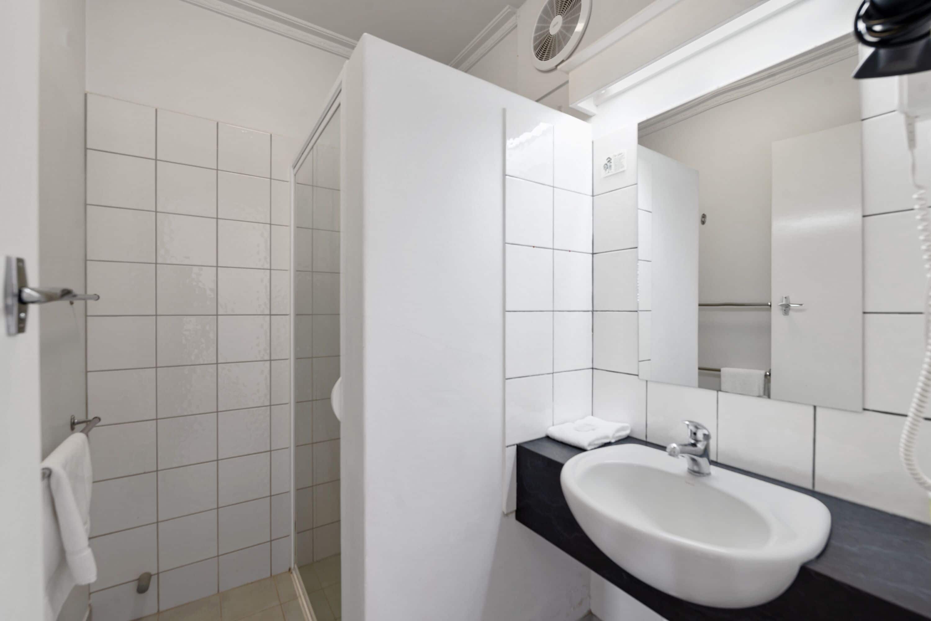 A modern bathroom with a white sink, a mirror, and a shower area.