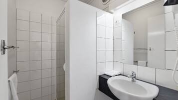 Un baño moderno con lavamanos blanco, un espejo y zona de ducha.