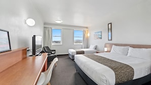 Habitación de hotel con dos camas, un escritorio, una silla, un televisor y ventanas amplias con vistas.