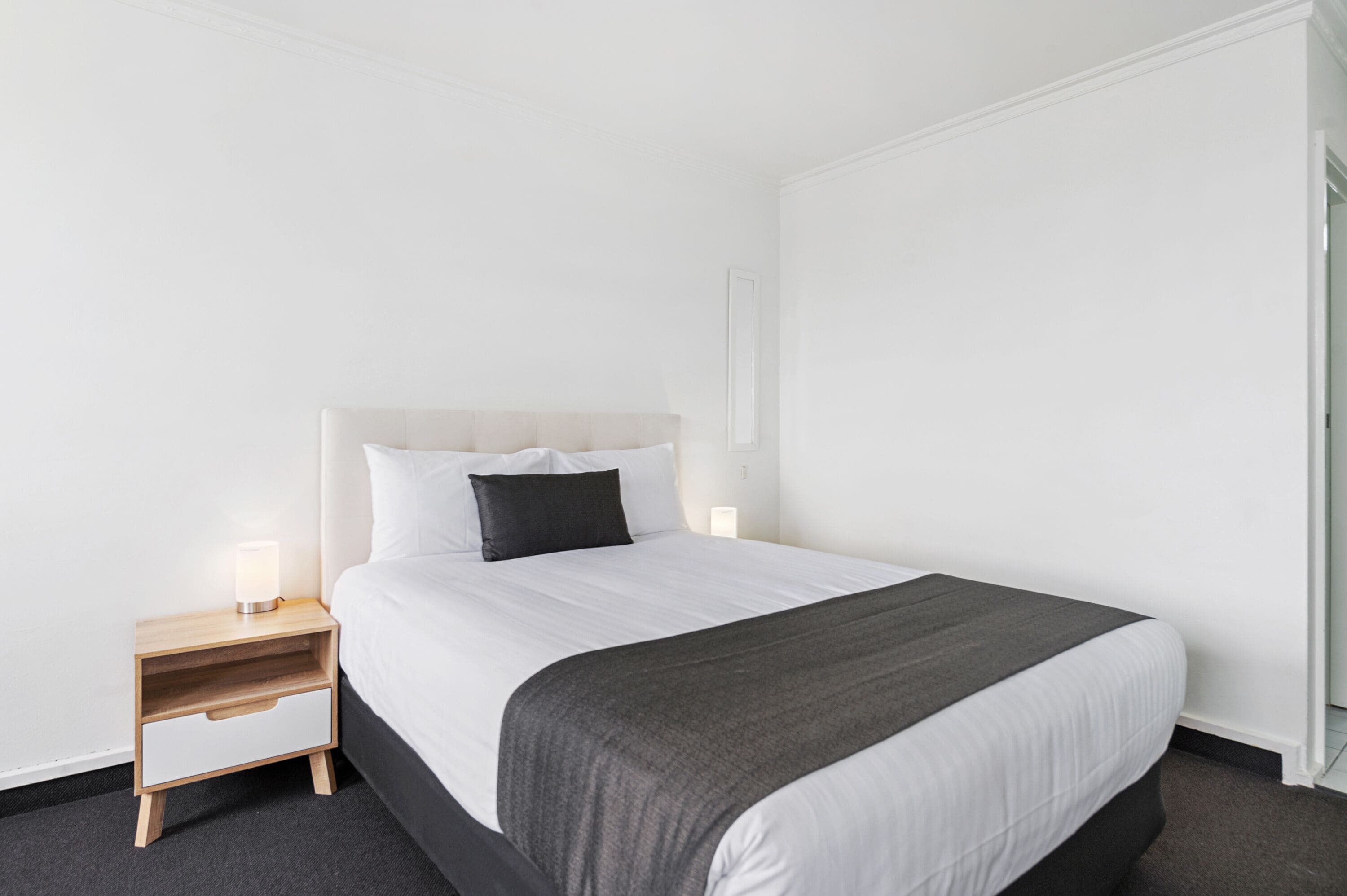 A hotel room with a bed, a nightstand with a lamp, and a wall-mounted light fixture.