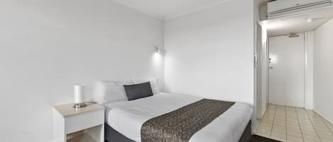 Una habitación de hotel moderna con una cama grande, una mesita de noche con lámpara y un equipo de aire acondicionado.