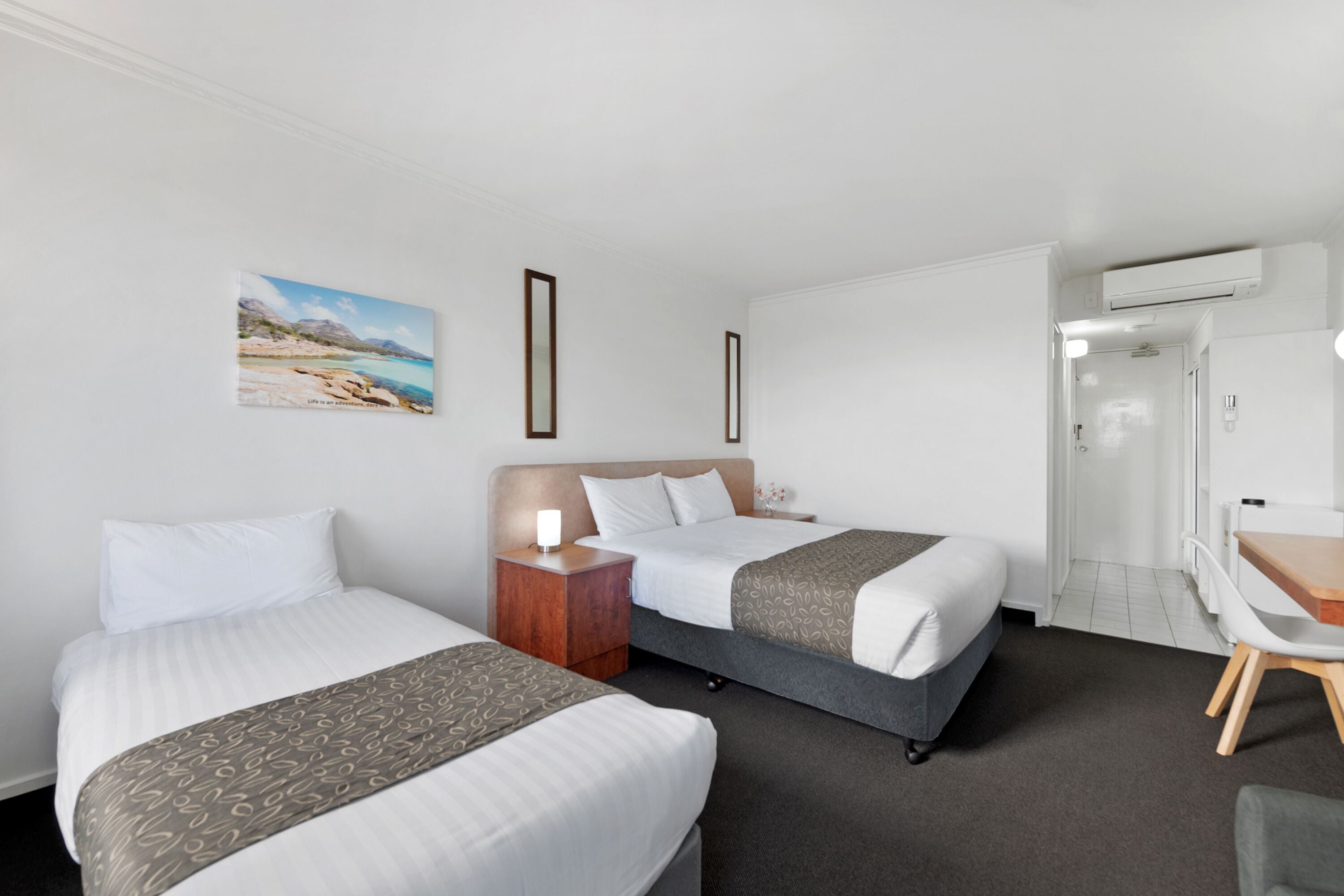 Habitación de hotel con dos camas, un escritorio, una silla y un cuadro en la pared.