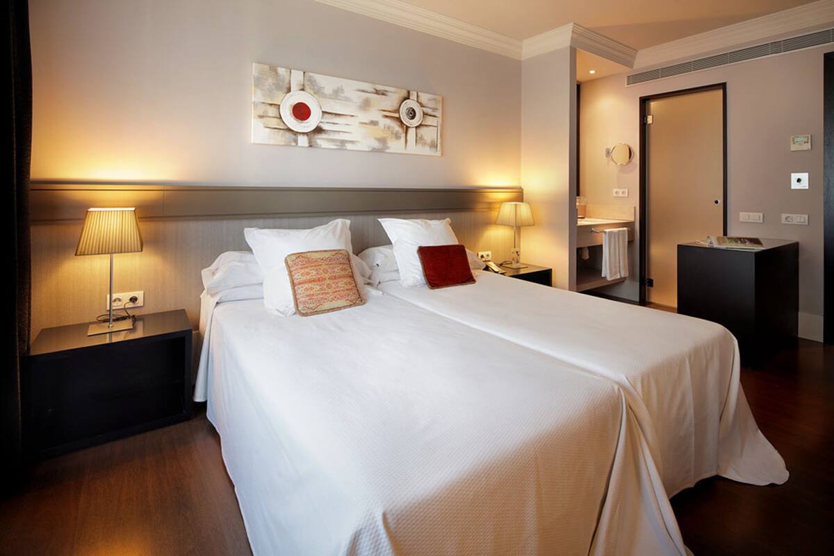 A hotel room with a large bed, two bedside tables with lamps, a wall-mounted artwork, and a door leading to a bathroom.
