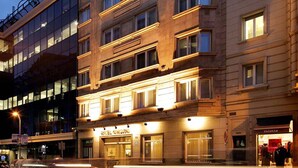 Un hotel de varios pisos con un diseño arquitectónico clásico, que presenta una bandera destacada en el techo y ventanas iluminadas.