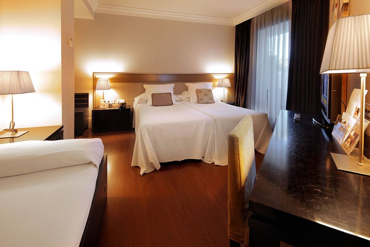 A hotel room with two beds, a desk, and a nightstand.