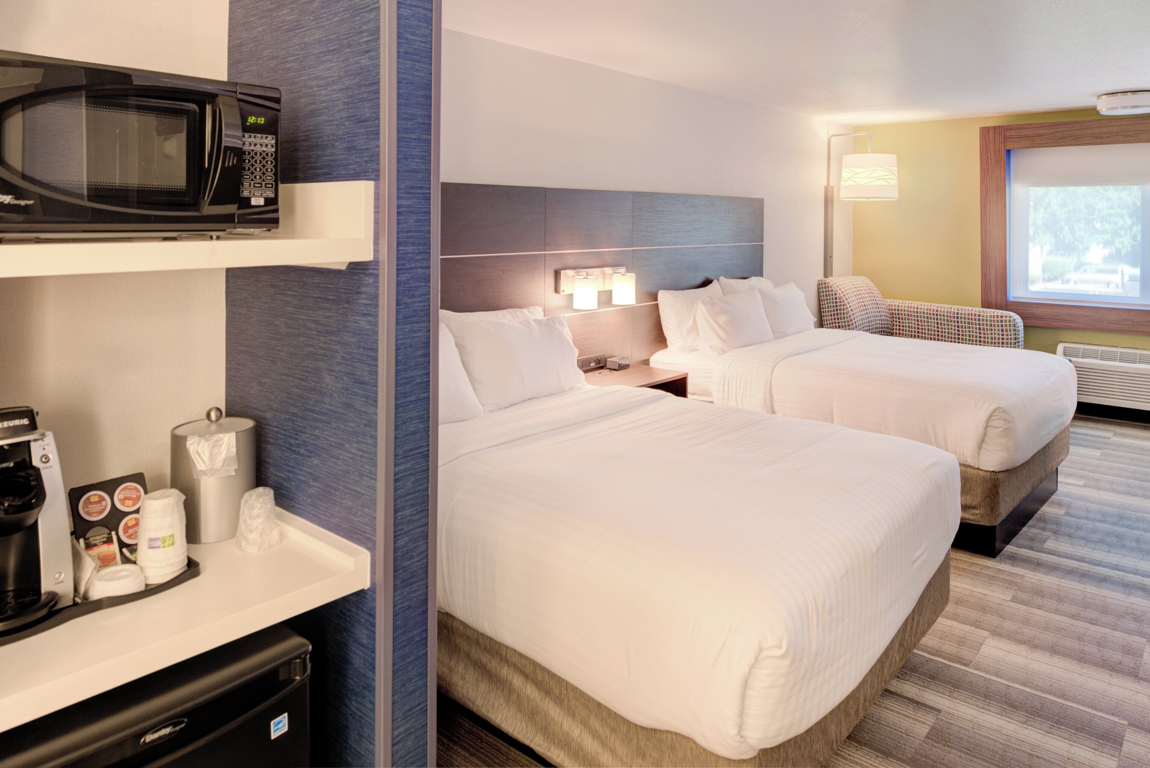 A hotel room with two beds, a microwave, a coffee maker, and a window with a view.