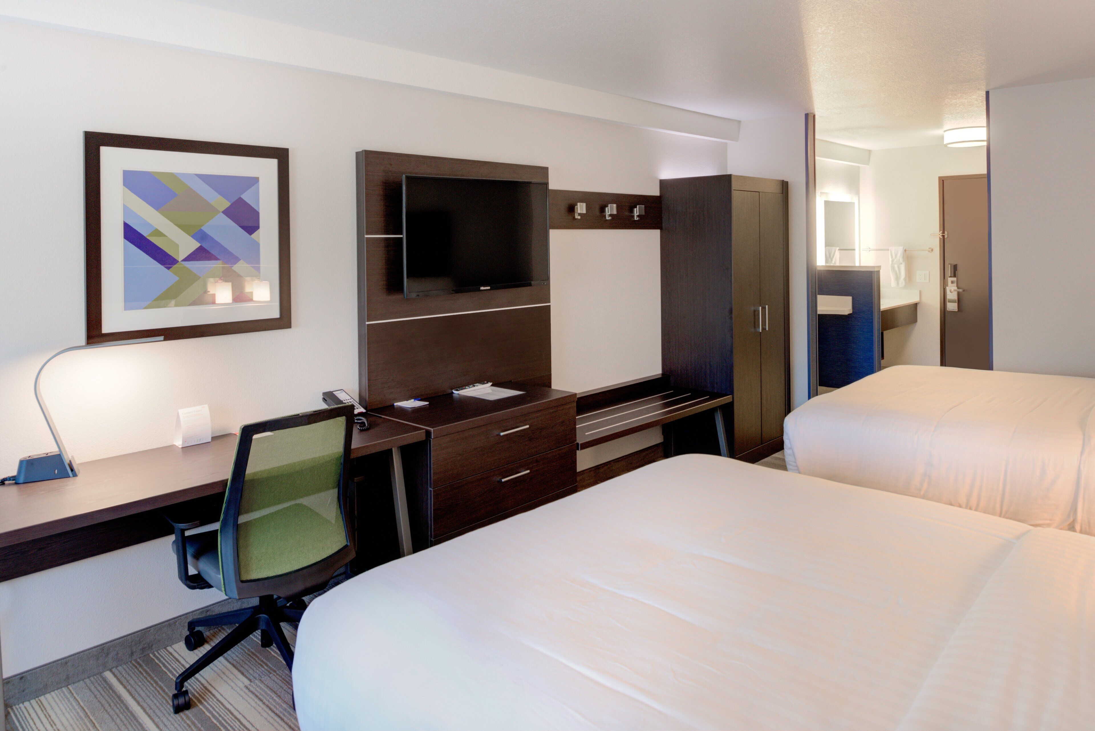 Una habitación de hotel con escritorio, televisión, armario y dos camas.