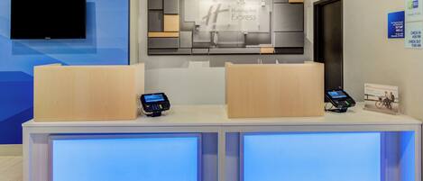 A hotel reception desk with a flat-screen TV, two card readers, and a sign for Holiday Inn Express.