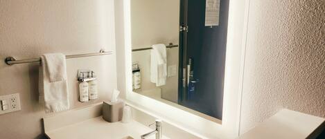 A modern bathroom with a large mirror, a white sink, and a towel rack.