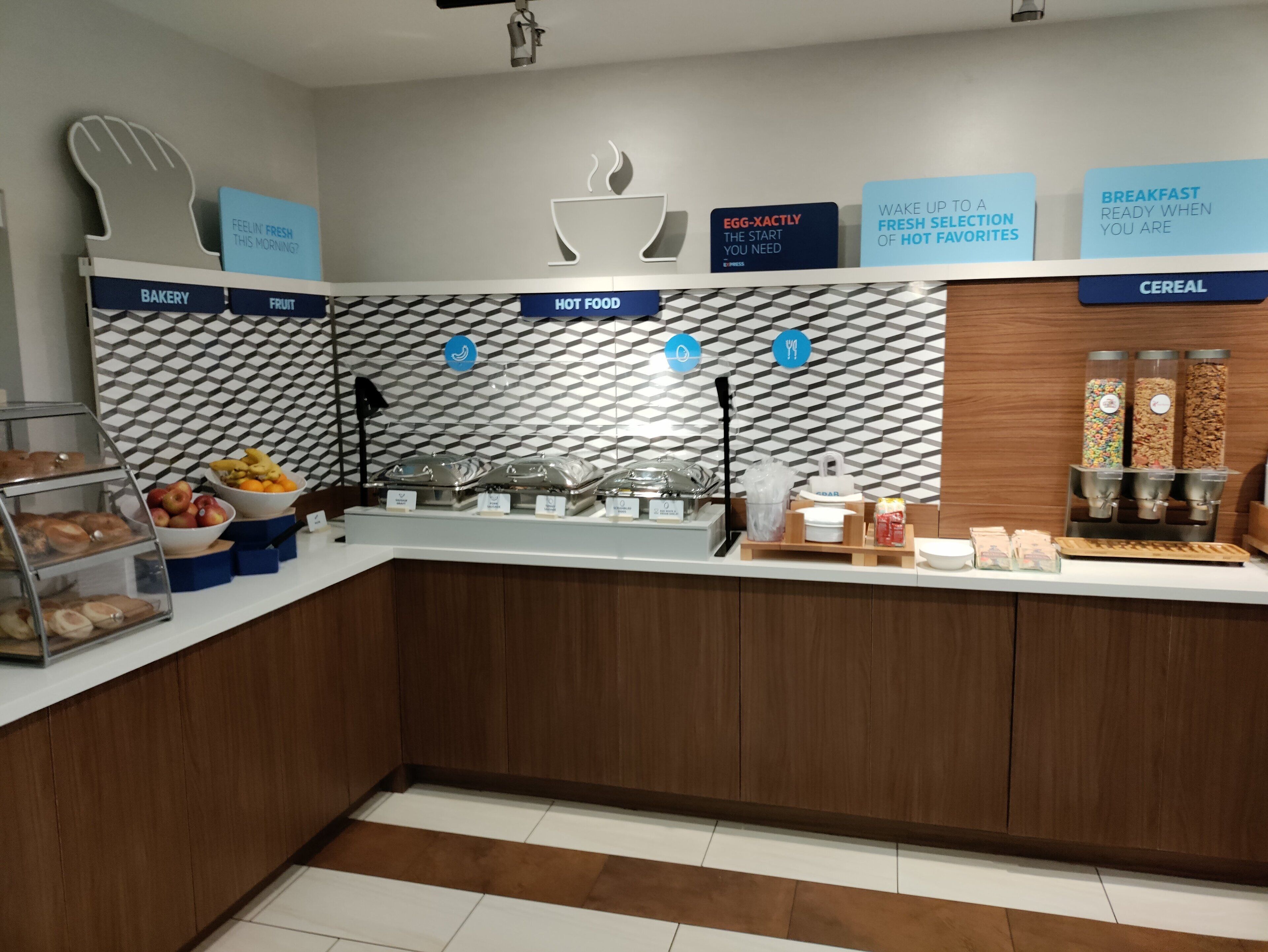 A modern breakfast bar with labeled sections for bakery, fruit, hot food, and cereal.