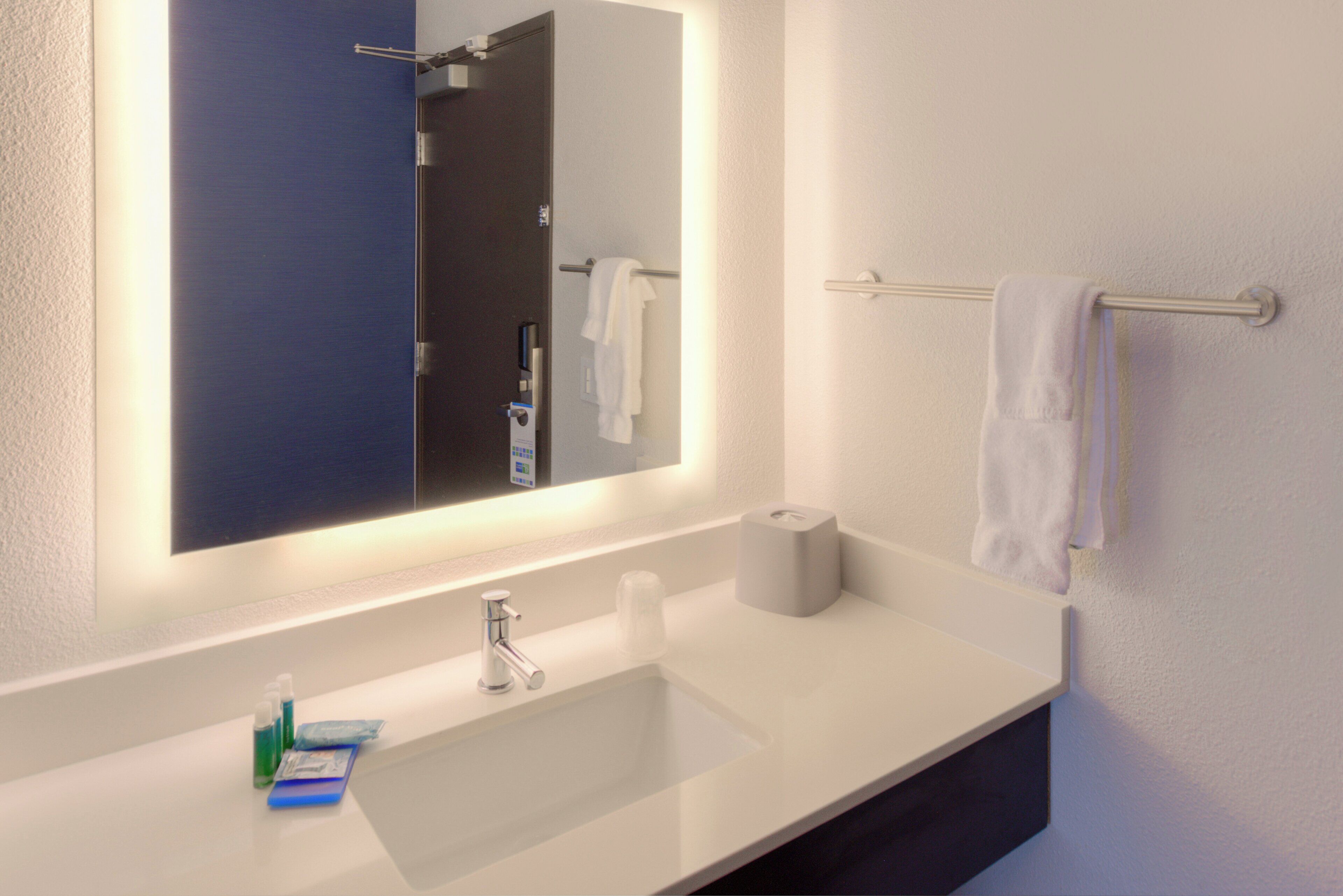 A bathroom with a white sink, a mirror, a towel rack, and a toilet paper dispenser.