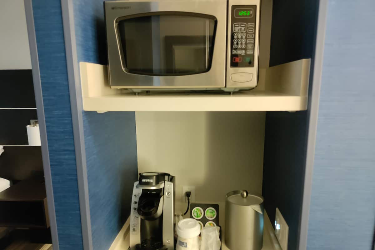 A kitchenette with a microwave, coffee maker, and coffee pods on the countertop.