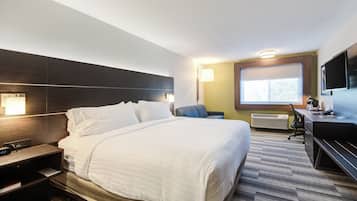 Habitació d'hotel amb un llit gran, una taula de nit, una làmpada i un escriptori amb una cadira.