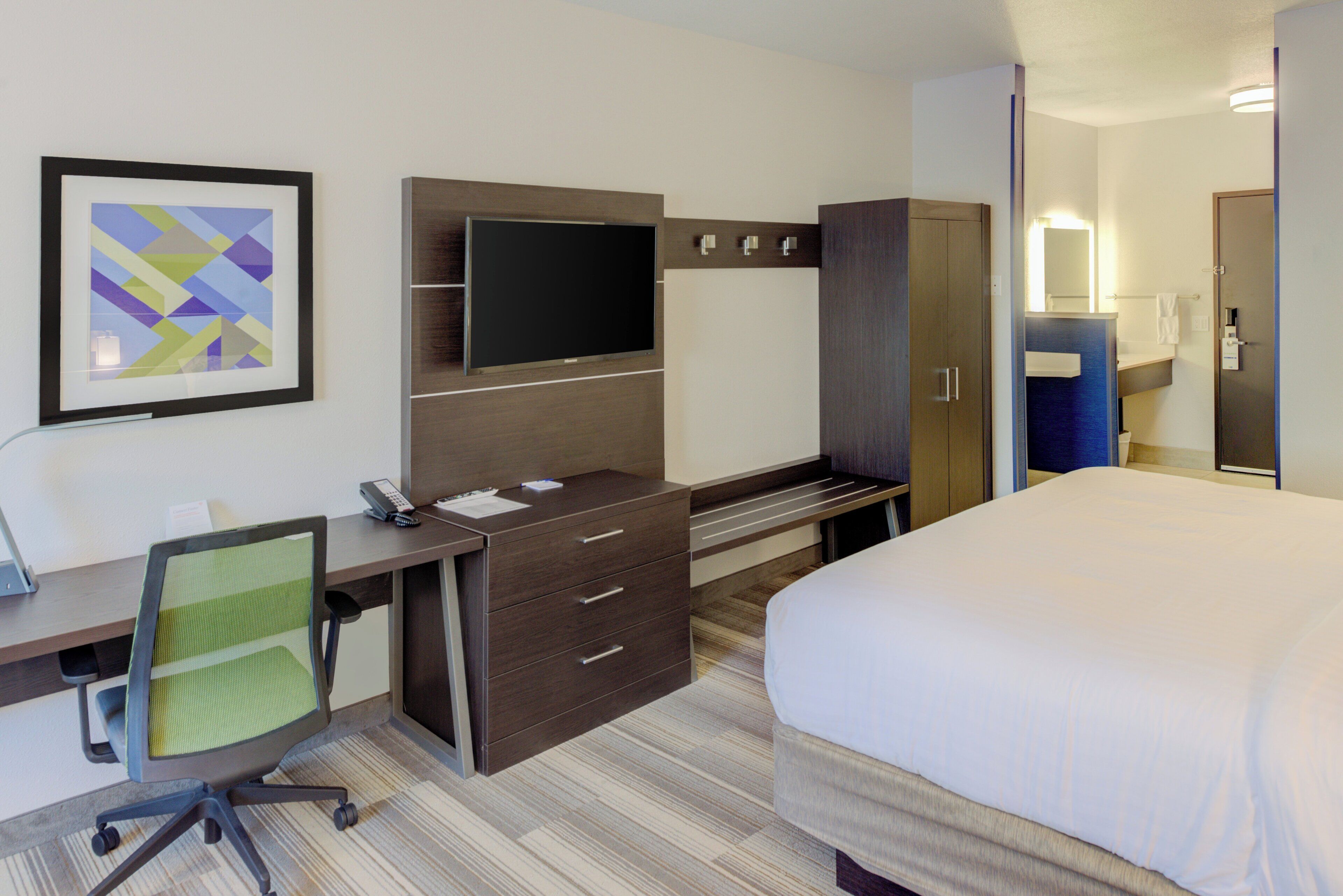 Ein Hotelzimmer mit Bett, Schreibtisch, Stuhl, Fernseher, Kleiderschrank und Bad.