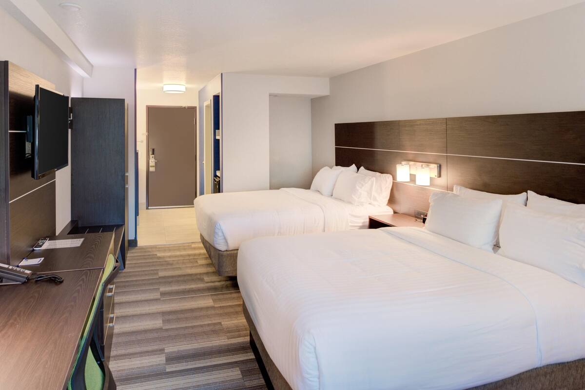 A hotel room with two beds, a desk, a TV, and a door leading to a bathroom.