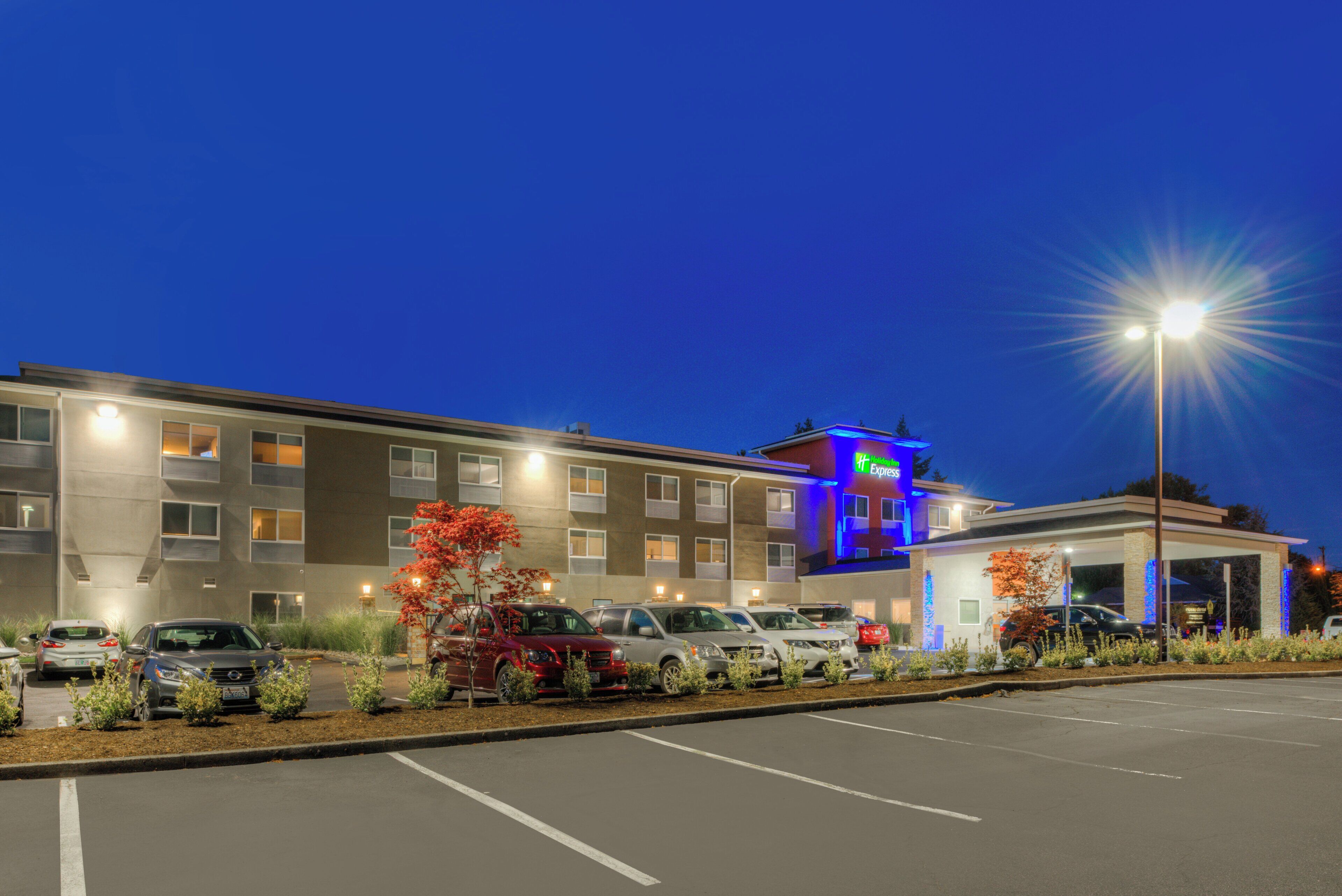 Un hôtel doté d’un parking, de plusieurs voitures et d’une façade bien éclairée.