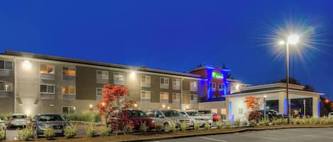 Un hôtel doté d’un parking, de plusieurs voitures et d’une façade bien éclairée.