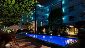 A nighttime swimming pool area with lounge chairs and a building in the background. - Cupertino Hotel (Cupertino)