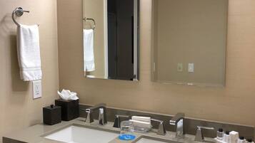 A hotel bathroom with two sinks, a mirror, a towel rack, and toiletries.