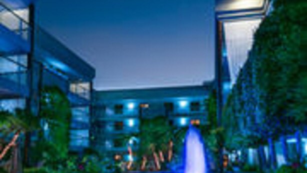 A fountain with water jets, surrounded by greenery and modern buildings. - Cupertino Hotel (Cupertino)