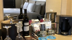 A hotel room with a bed, a minibar, a coffee maker, wine bottles, and a tray with glasses and napkins. - Cupertino Hotel (Cupertino)