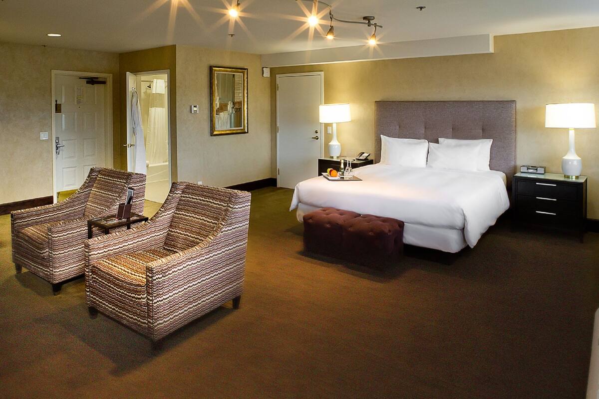 A hotel room with a bed, two bedside lamps, a nightstand, a chair, and a mirror.