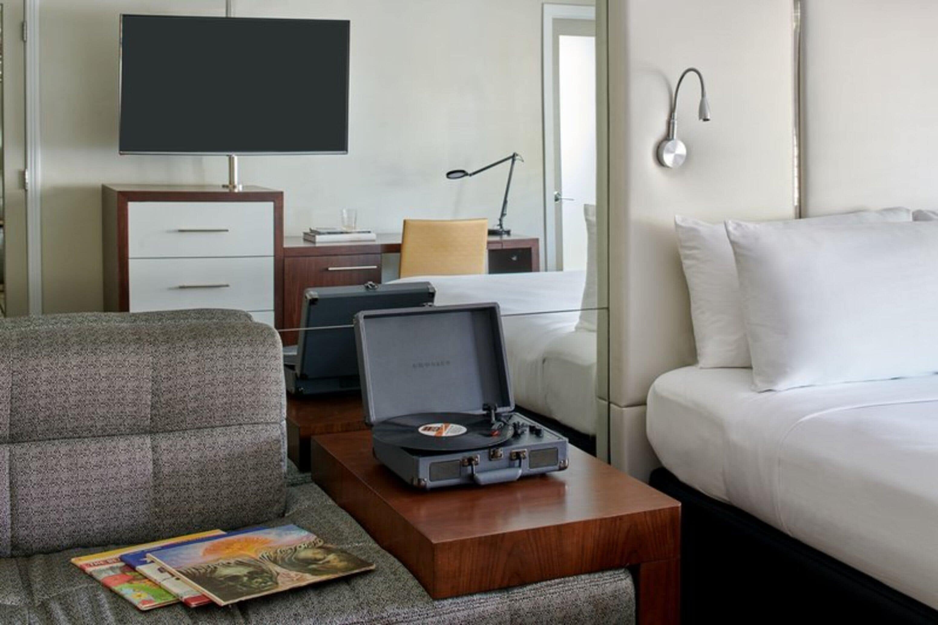 Habitación de hotel con cama, escritorio, computadora portátil, tocadiscos, televisor y silla.