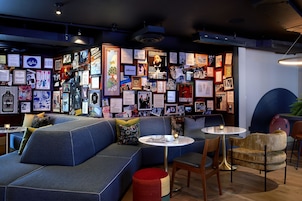 Un área de descanso moderna con un sofá azul, mesas redondas y una pared decorada con cuadros y carteles.