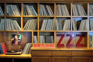 A music store with vinyl records on shelves and a 'NOW PLAYING' sign.
