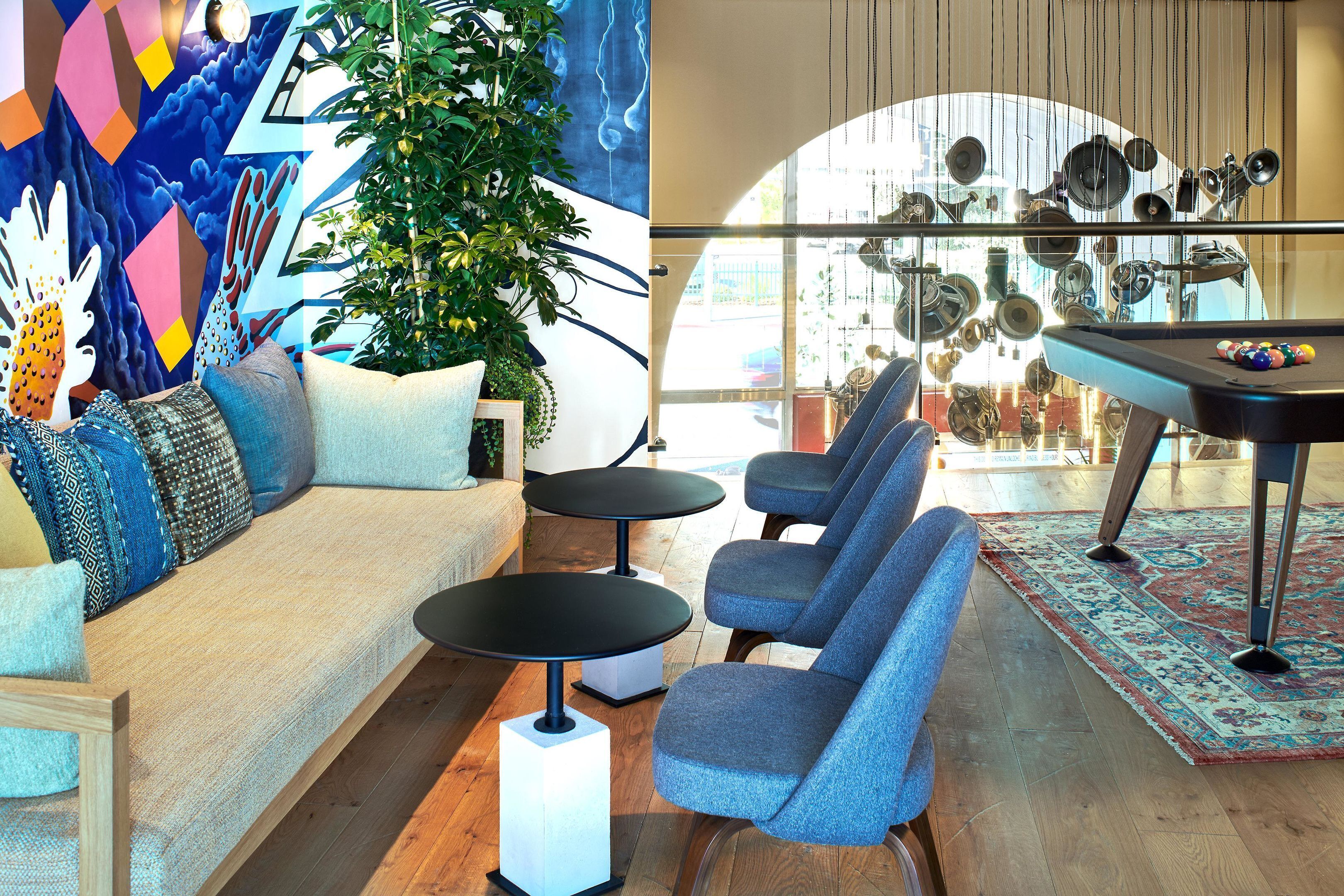 A modern living room with a sofa, two armchairs, a coffee table, a pool table, and a large window with a view of the city.