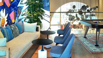 A modern living room with a sofa, two armchairs, a coffee table, a pool table, and a large window with a view of the city.