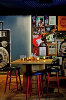 Zona de bar con taburetes, una mesa, vasos y carteles en la pared.