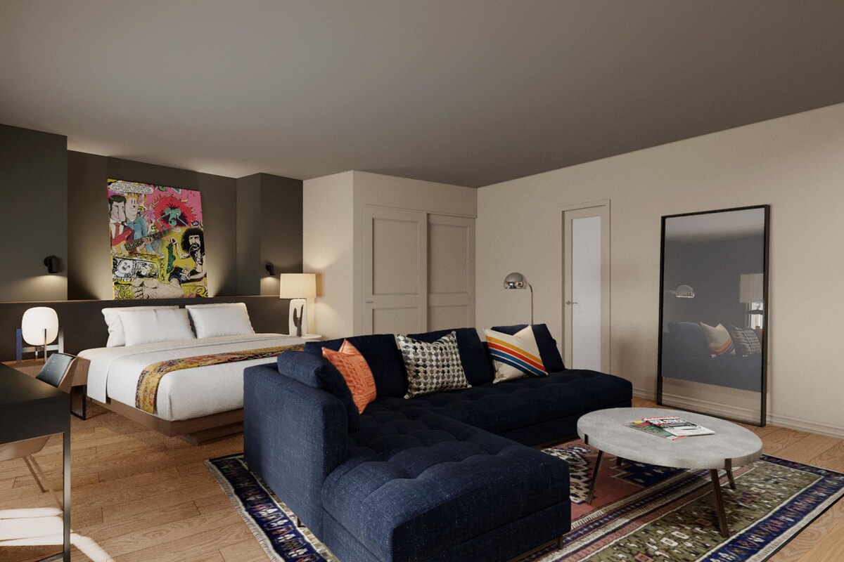 A modern hotel room with a bed, a sofa, a coffee table, a lamp, and a large mirror.