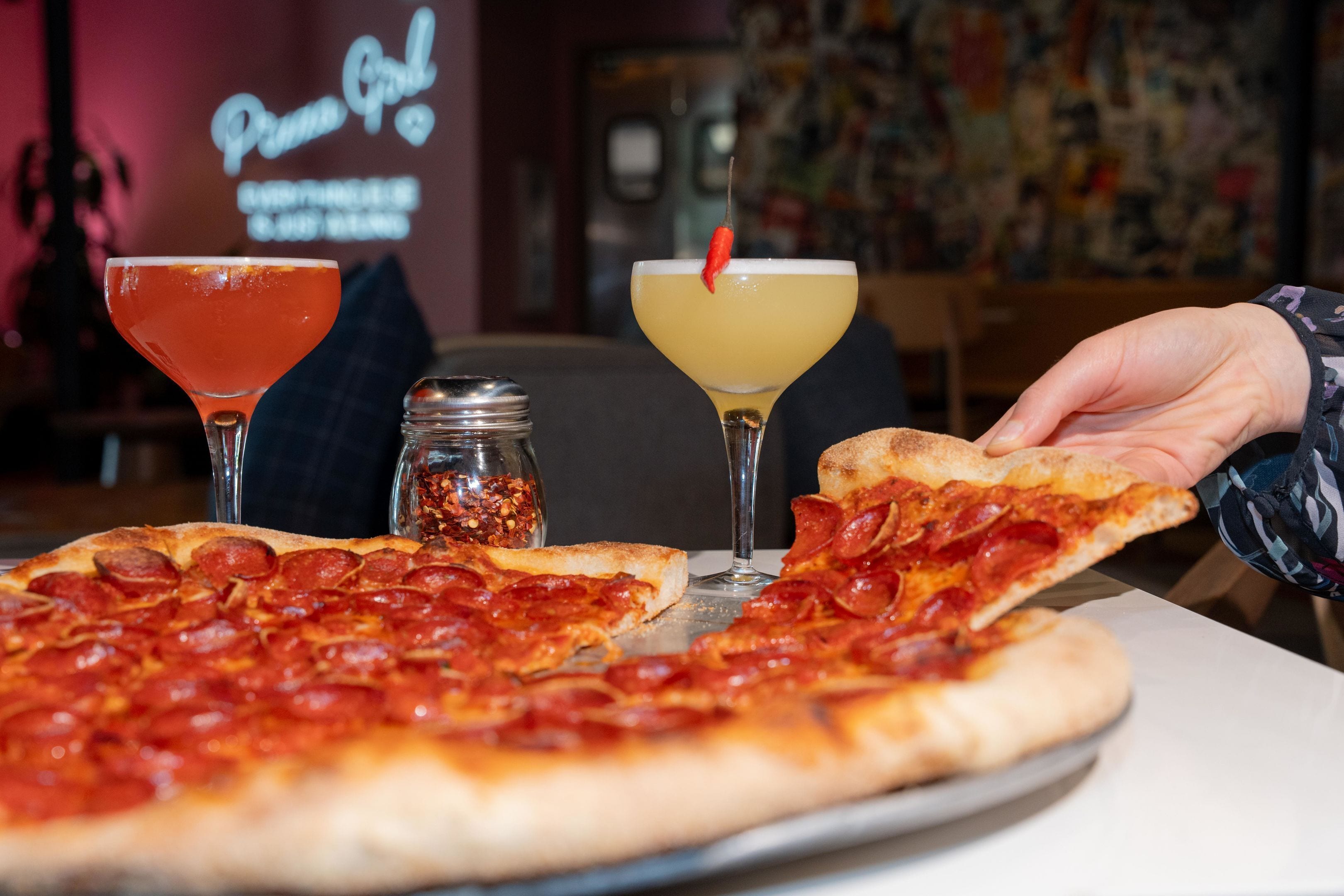 A pizza with pepperoni, a martini, and a cocktail with a red chili garnish on a table.