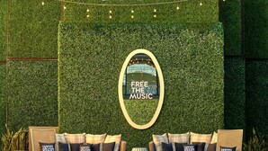 Zona de piscina con pared verde, un cartel que dice 'FREE HEAR MUSIC' y asientos de descanso con almohadones que dicen 'HOTEL ZIGZAG'.