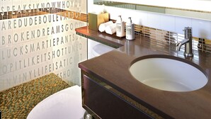 A bathroom with a large mirror, a sink, and a toilet. The walls have text and patterns. - Hotel Ziggy on Sunset (West Hollywood)