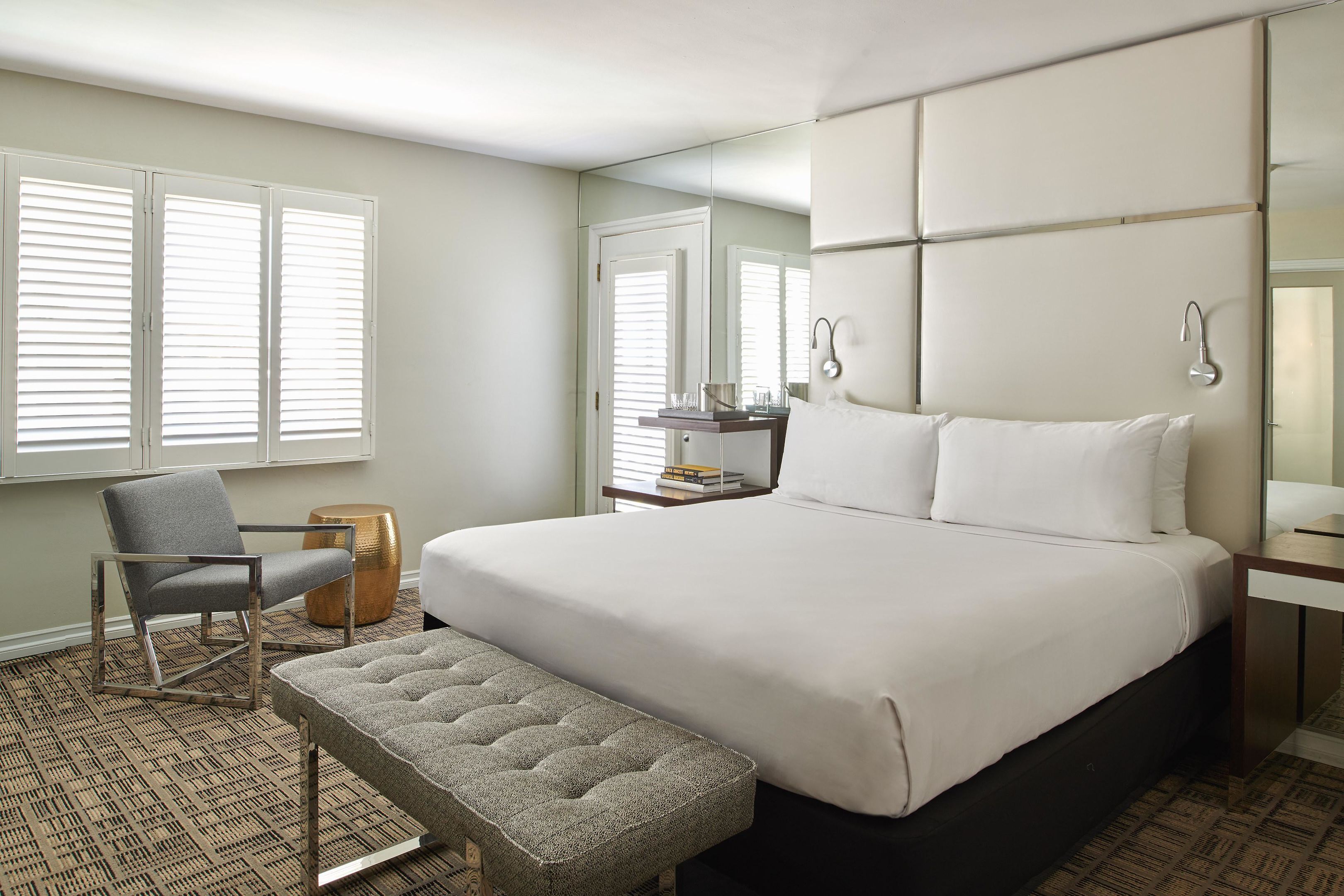 A hotel room with a large bed, a chair, a bench, a desk, and a mirror.