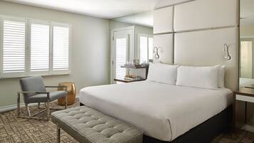 A hotel room with a large bed, a chair, a bench, a desk, and a mirror.